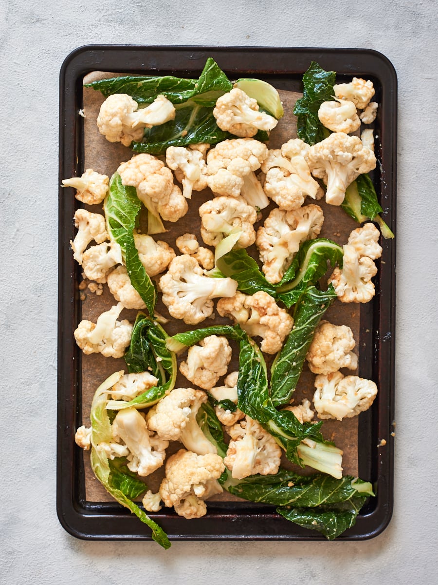 raw cauliflower and leaves on tray with miso coating mixed