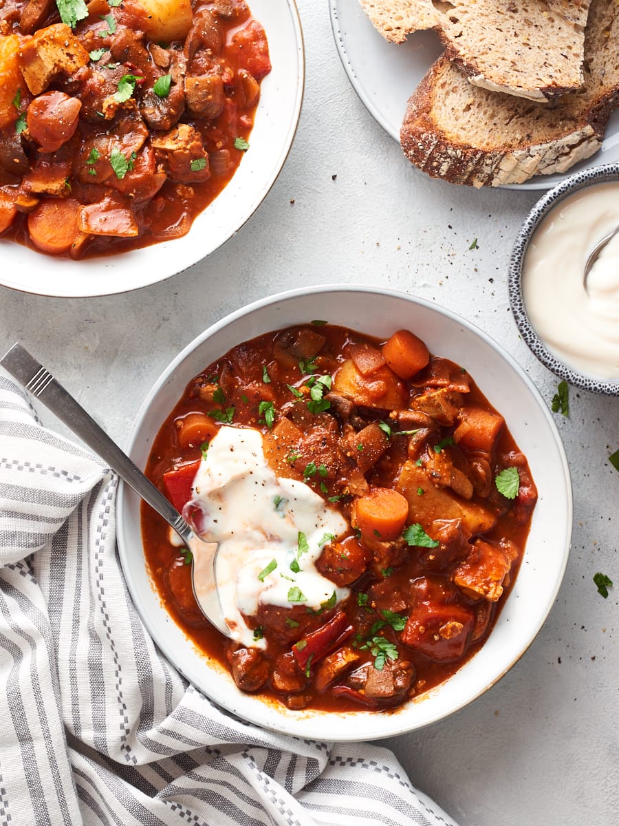 Two bowls of vegan goulash photographed from overhead with yoghurt