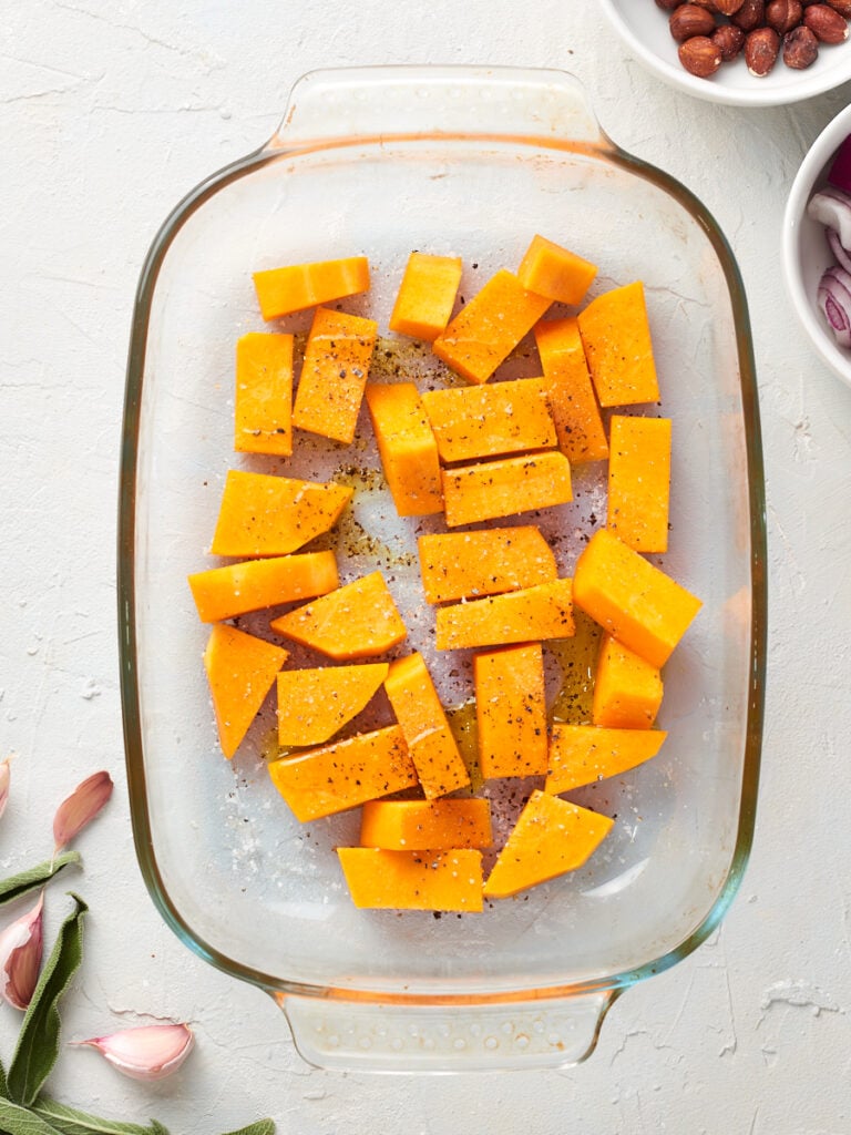 raw butternut squash in baking dish with oil and seasoning