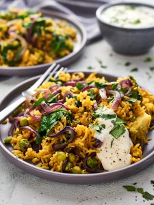 Two plates of green biryani with yoghurt in the background