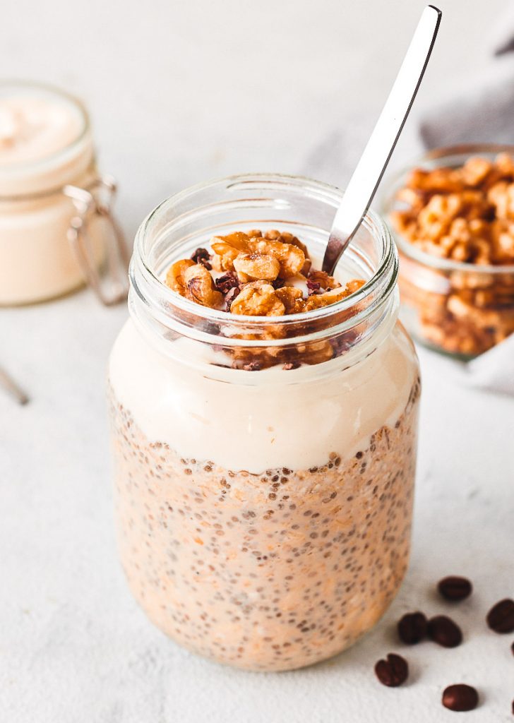 Mason jar of coffee overnight oats with long spoon, yoghurt, and walnuts
