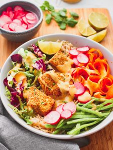 Bowl of tofu katsu salad with lime, coriander, and pickled radish on the side