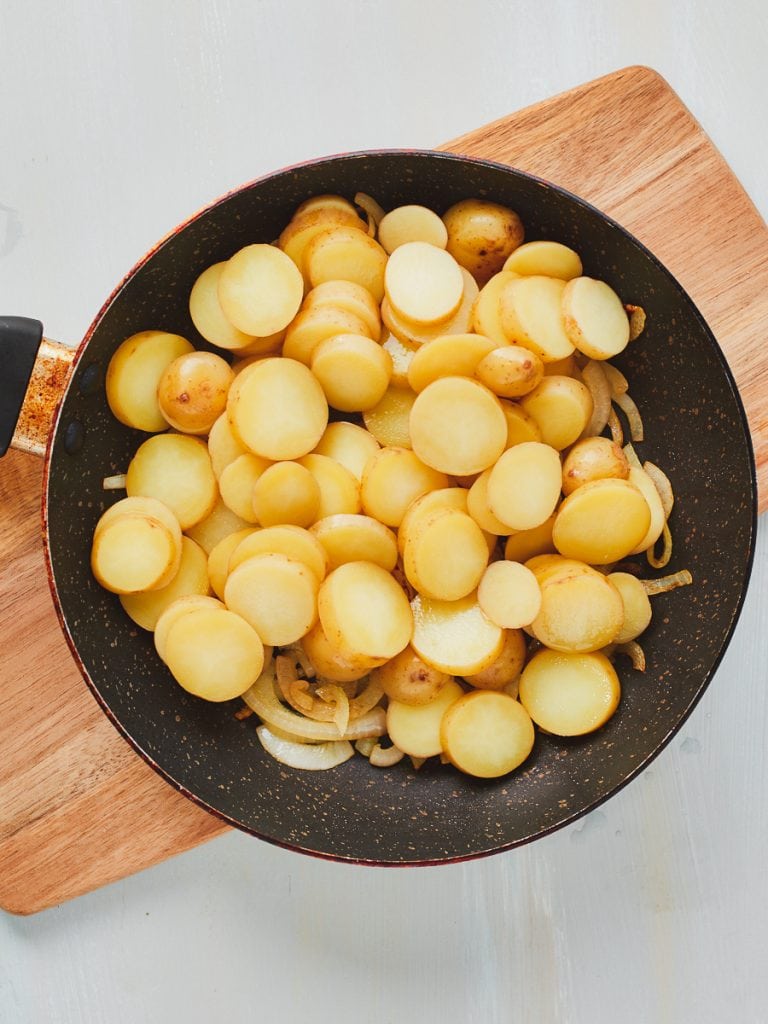 Adding parboiled potatoes to the frying pan with onion