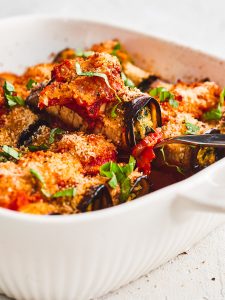 An eggplant cannelloni being lifted out of the oven dish
