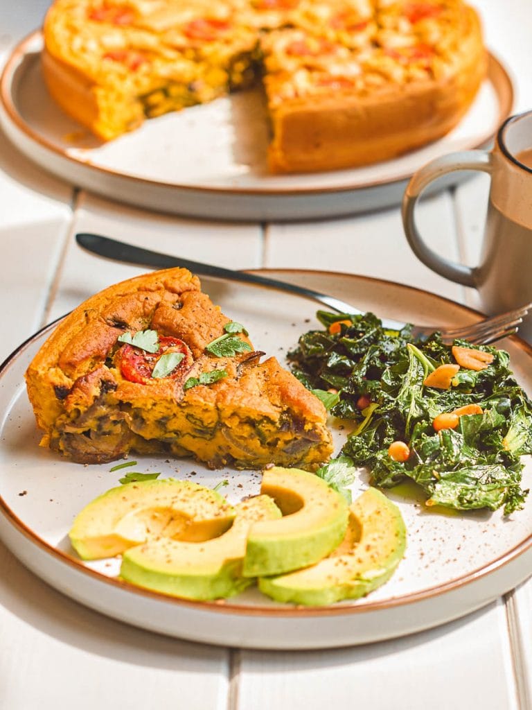 A slice of vegan frittata on a plate with sauteed kale and avocado