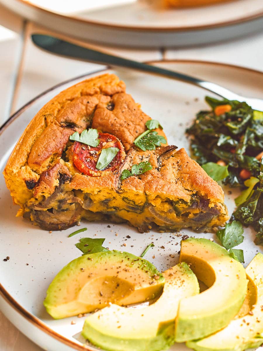 Slice of vegan frittata on a plate with avocado and sauteed kale