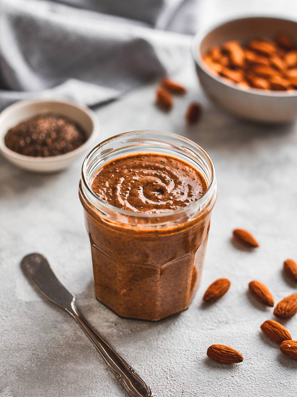 Almond and chia seed butter in a jar with a bowl of almonds and chia seeds behind