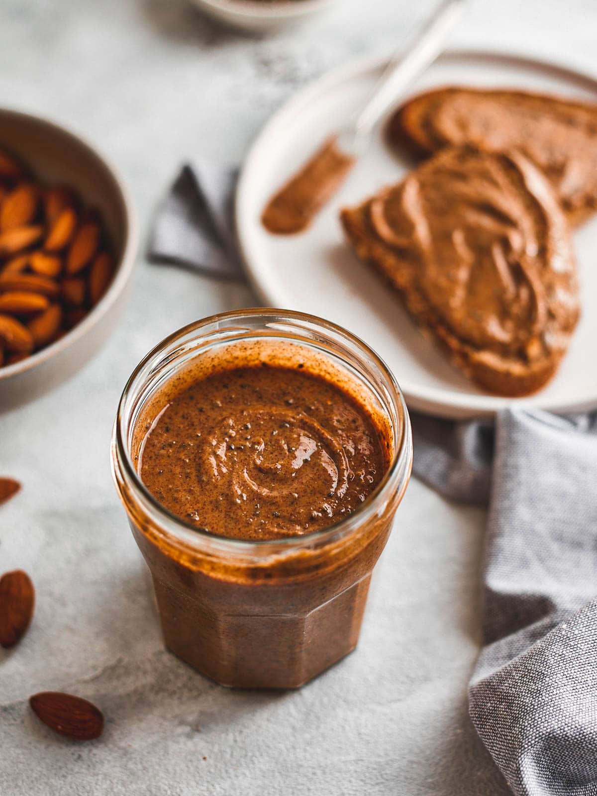 Almond chia seed butter in a jar with toast and a bowl of almonds behind it