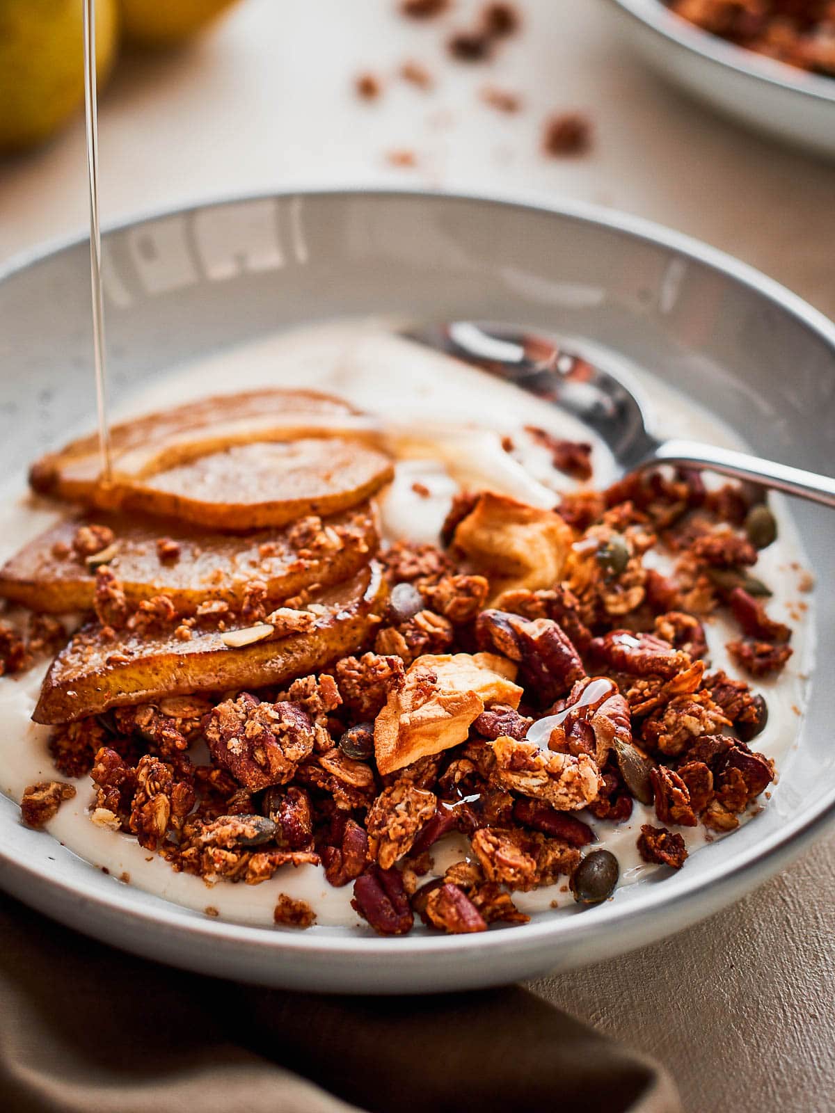 Close up photograph of a bowl of pear granola with a maple syrup drizzle