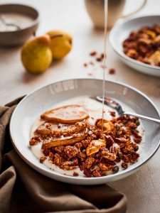 Maple syrup being drizzled onto a bowl of pear granola