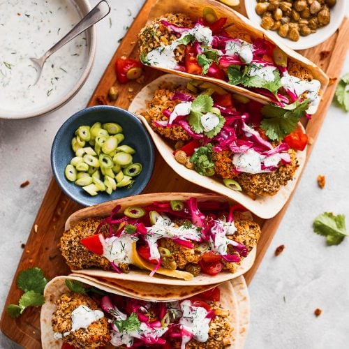 Four vegan fish tacos lined up on a chopping board with toppings