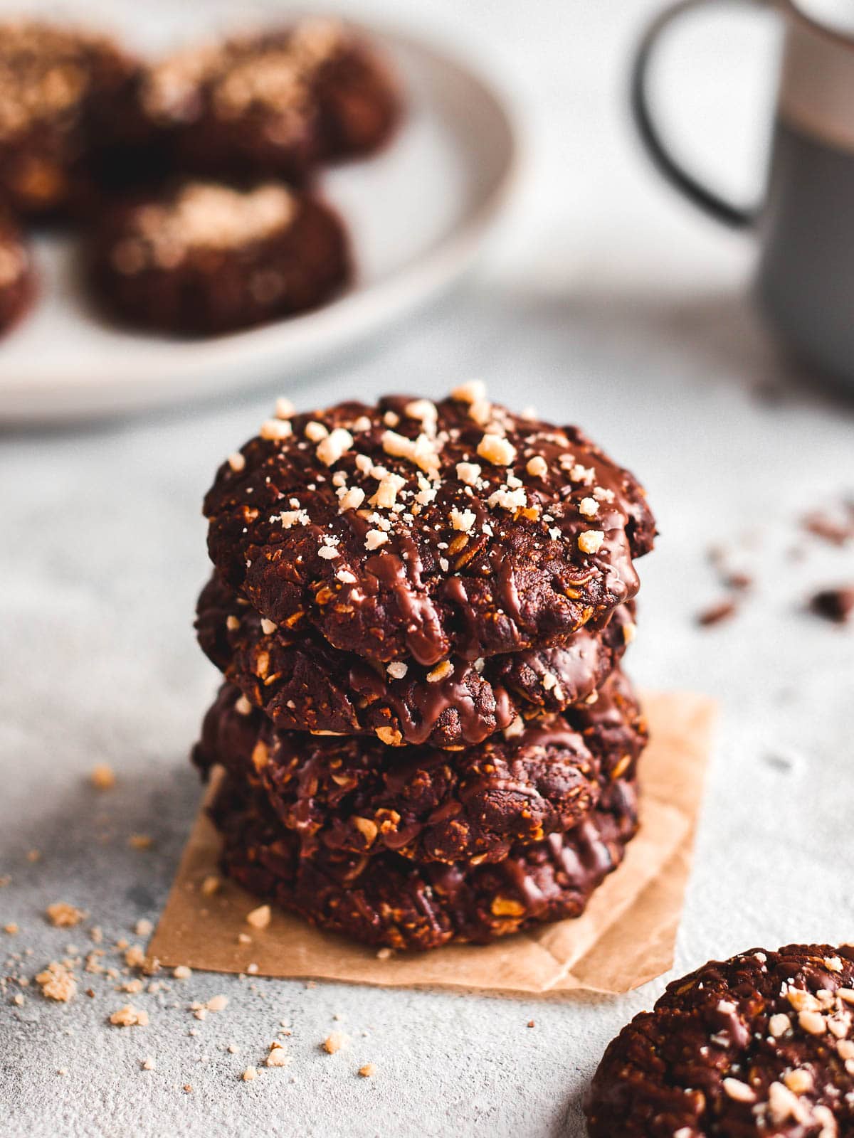 A stack of vegan chocolate oatmeal cookies with a plate of cookies and a mug behind