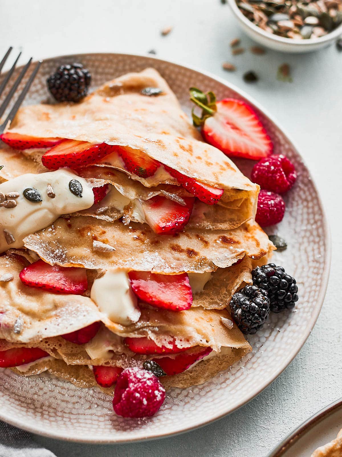 Close up photo of A plate with 3 coconut milk crepes filled with berries and yoghurt
