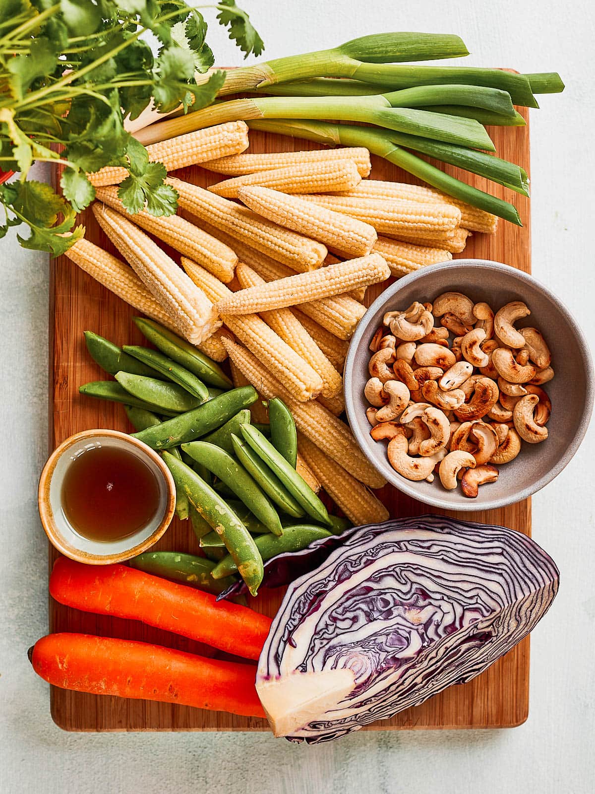 Ingredients for baby corn salad- baby corn, spring onions, cilantro, mangetout, cashews, sesame oil, carrots and red cabbage