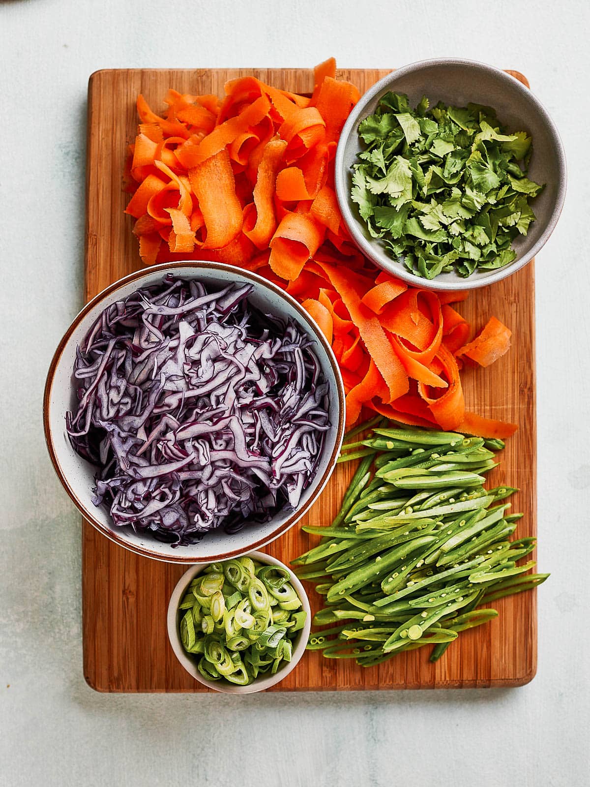 Shredded and chopped carrot, spring onion, cilantro, red cabbage and mangetout on a chopping board