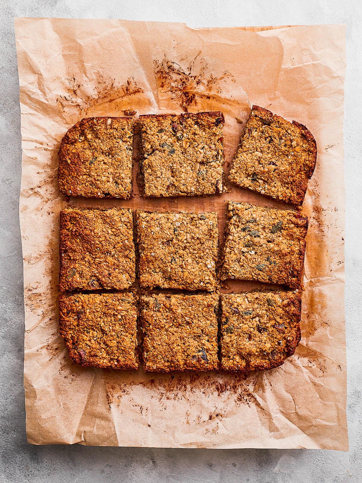 Overhead photo of a tray of baked date flapjacks chopped up into 9 squares on baking paper