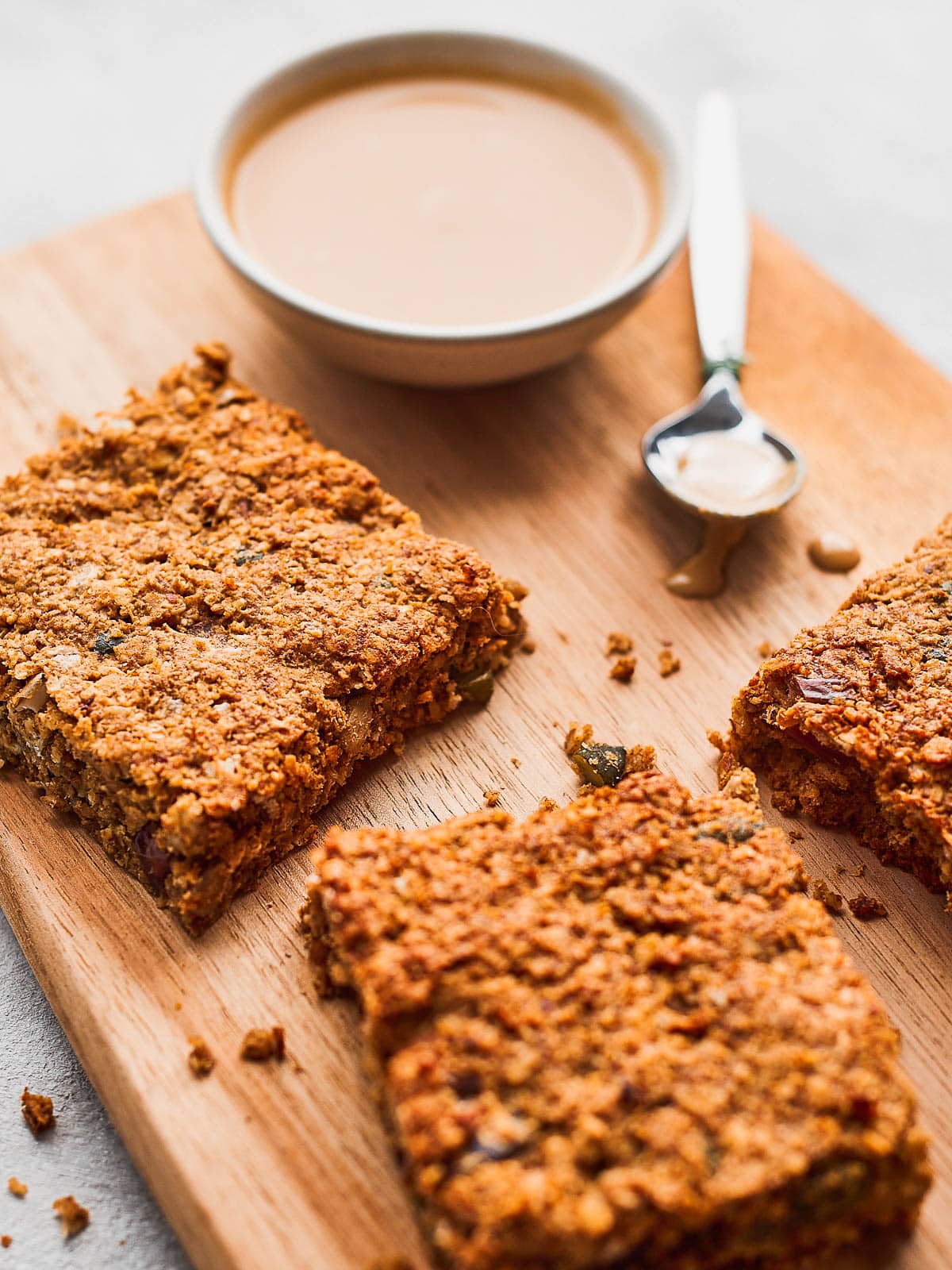 Close up photo of 3 squares of date flapjacks with a small bowl of tahini