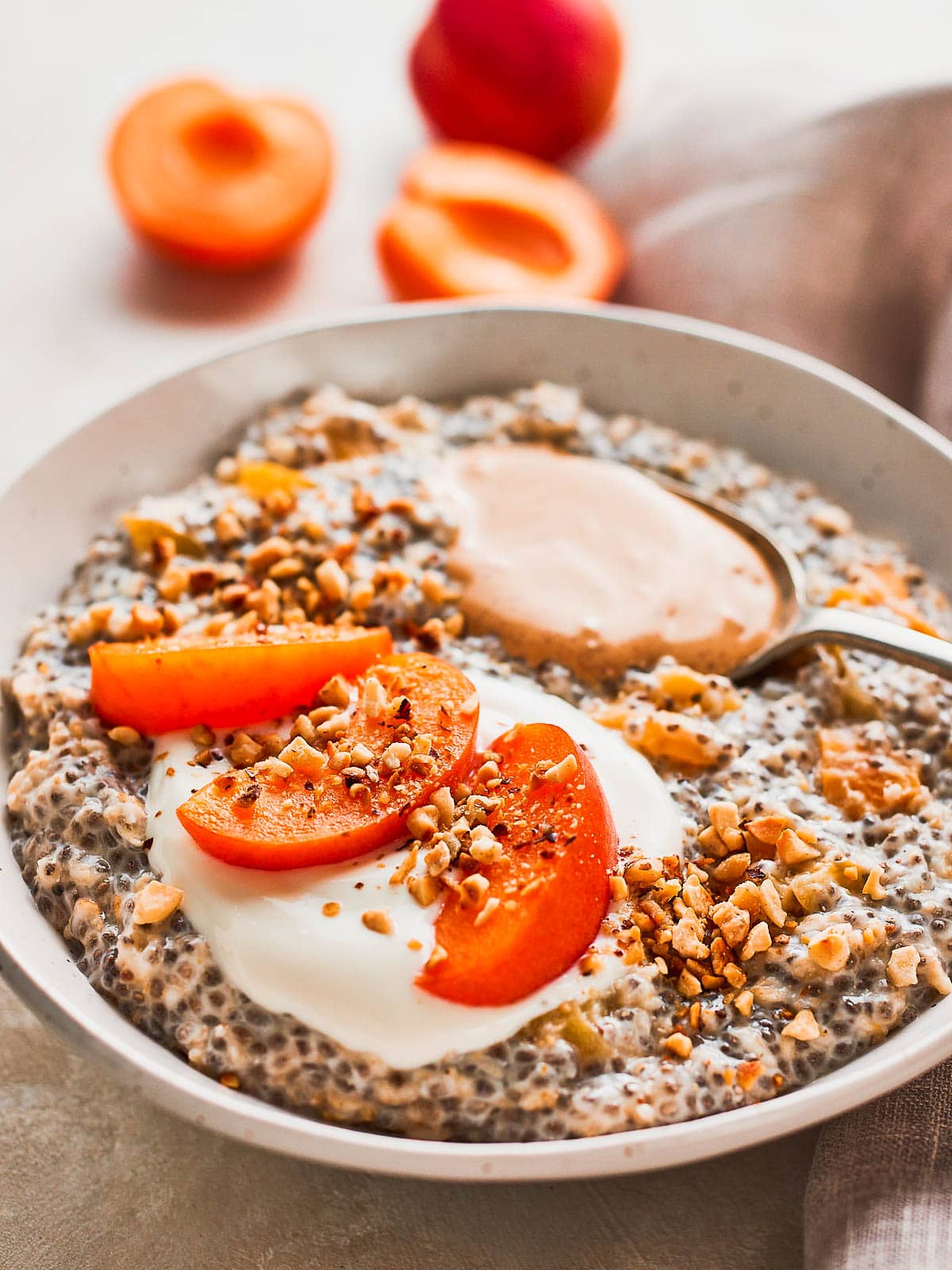 Close up three quarter shot of a bowl of chia seed porridge, topped with yoghurt, almond butter, chopped nuts, and three wedges of apricot